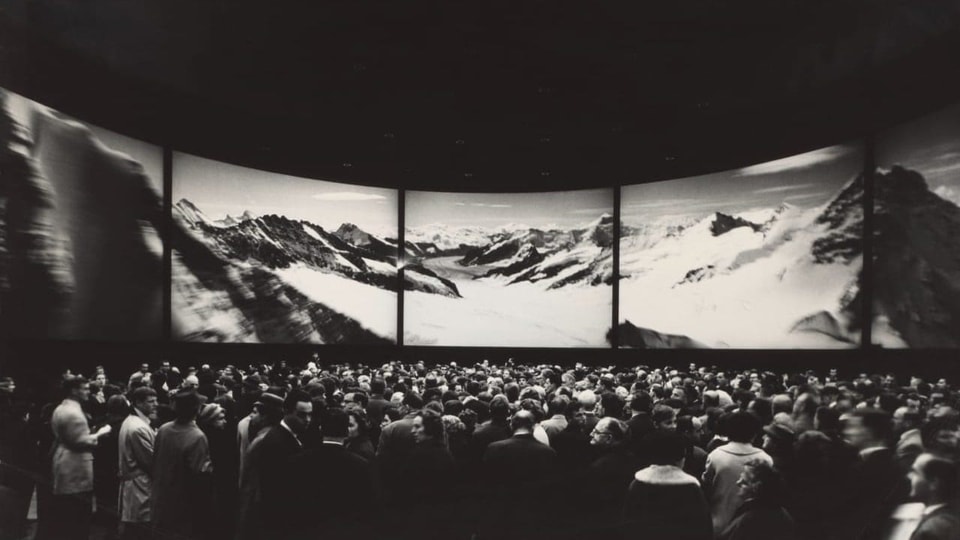 Schwarz-Weiss Bild von einer Menschenmenge vor einem riesigen Panorama-Bild
