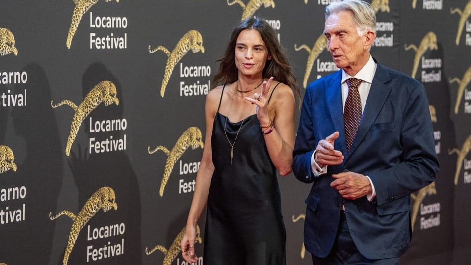 Eine Frau und ein Mann sind im Gespräch und laufen vor einer Wand mit bedrucktem Filmfestival-Locarno-Logos.