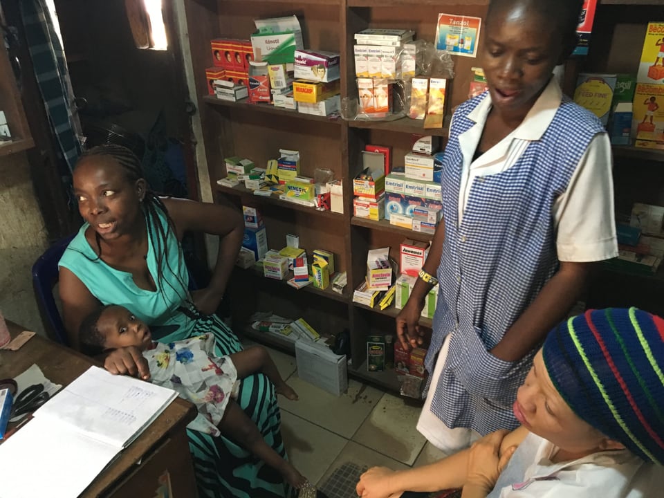 Drei Afrikanerinnen, ein hält ein Baby vor einem Gestell mit Medikamenten.