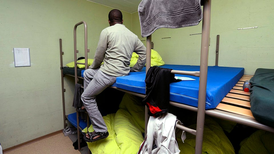 Asylbewerber auf Etagenbett sitzend in Zivilschutzanlage