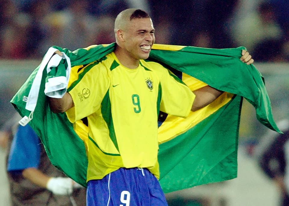 Ronaldo mit einer brasilianischen Flagge um die Schultern. Der Kopf ist rasiert, vorn steht nur noch ein Haar-Dreieck.