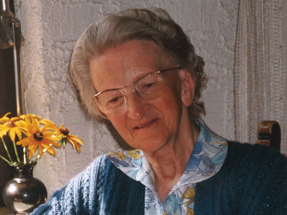 Die Seniorin sitzt vor einer Vase mit gelben Blumen.