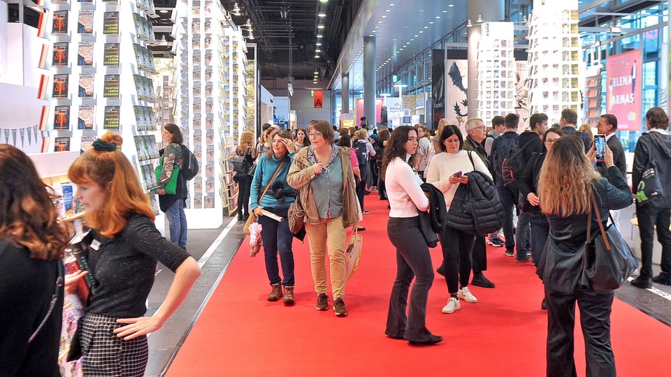 Exhibition hall red carpet, high shelves displaying books and lots of guests looking around