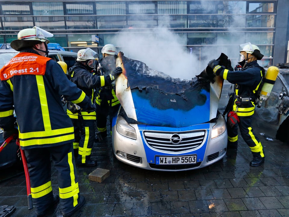Feuerwehrleute löschen ein brennendes Polizeiauto. (reuters)