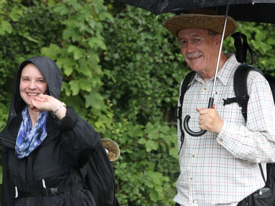 Frau und Mann wandern im Regen. Der Mann hat einen Schirm.