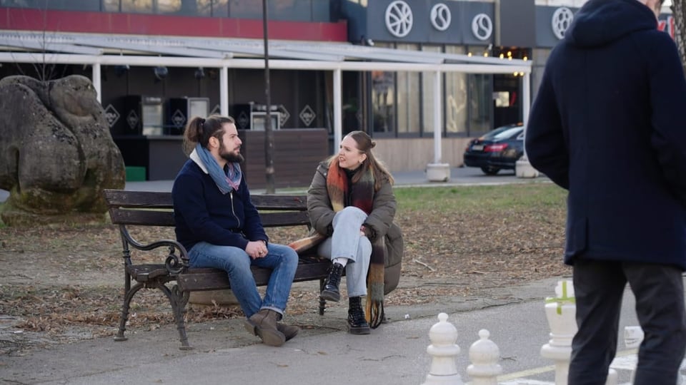 Moderatorin und Protagonist sitzen auf einer Bank in einem Park