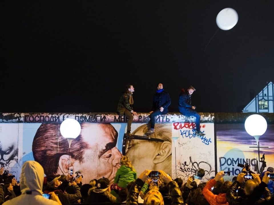 Menschen stehen vor Überresten der Berliner Mauer.