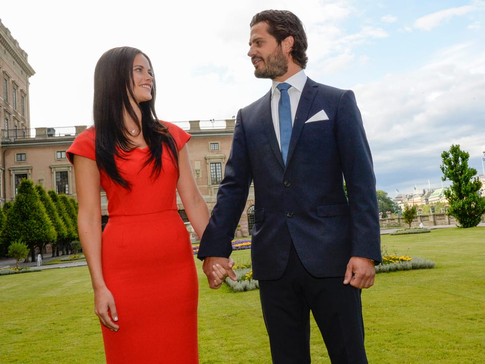 Sofia Hellqvist in einem roten Kleid hält die Hand von Carl Philip. Die beiden stehen in einem Schlosspark.