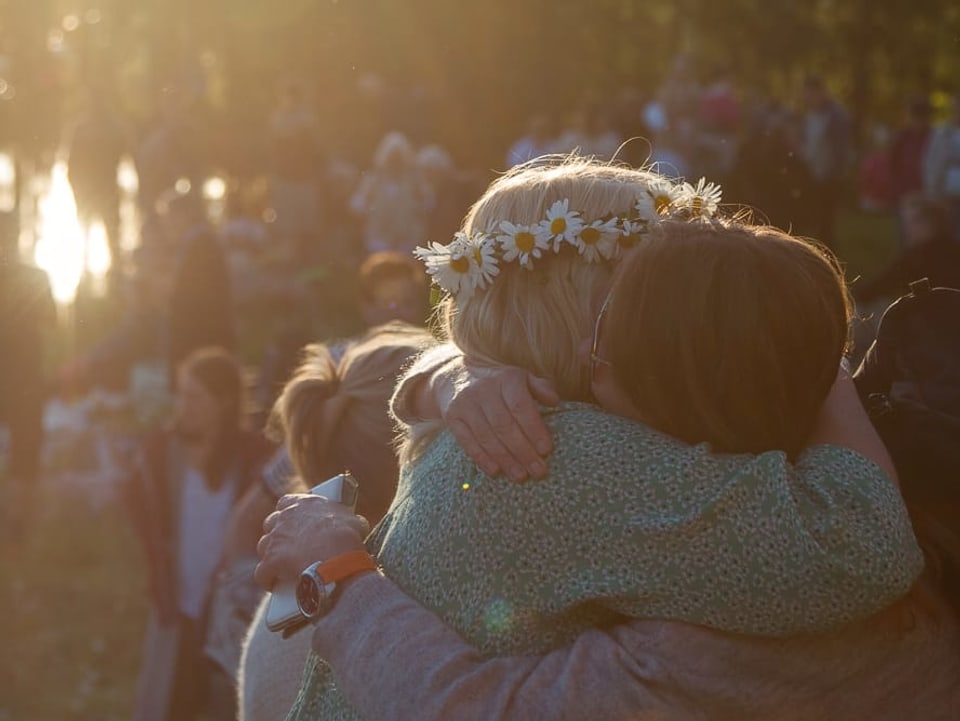 Zwei Frauen umarmen sich innig an einem Fest, eine trägt einen Blumenkranz in den Haaren.