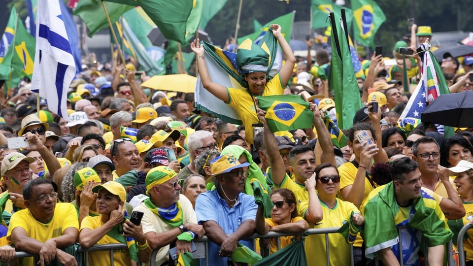 Menschen in gelben Brasilientrikots stehen auf der Strasse und schwenken Flaggen.