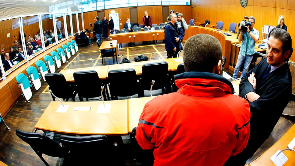 Der angeklagte ehemalige deutsche Söldner der IS-Terrormiliz Kreshnik B. in roter Jacke steht im Oberlandesgericht Frankfurt mit dem Rücken zum Forografen. Neben ihm steht sein Anwalt.