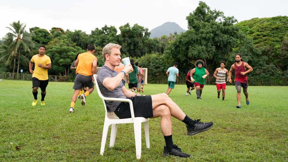Thomas Rongen (Michael Fassbender) sitzt cool auf einem Stuhl mitten auf dem Rasen, während seine Spieler arg schwitzen.