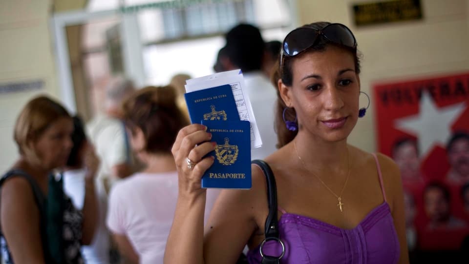Eine Kubanerin hält lächelnd zwei Reisepässe in die Höhe.