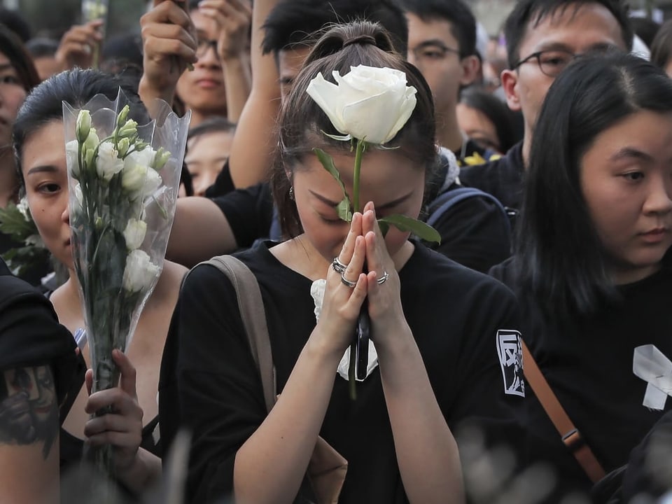 Trauernde Protestierende halten Blumen in den Händen.