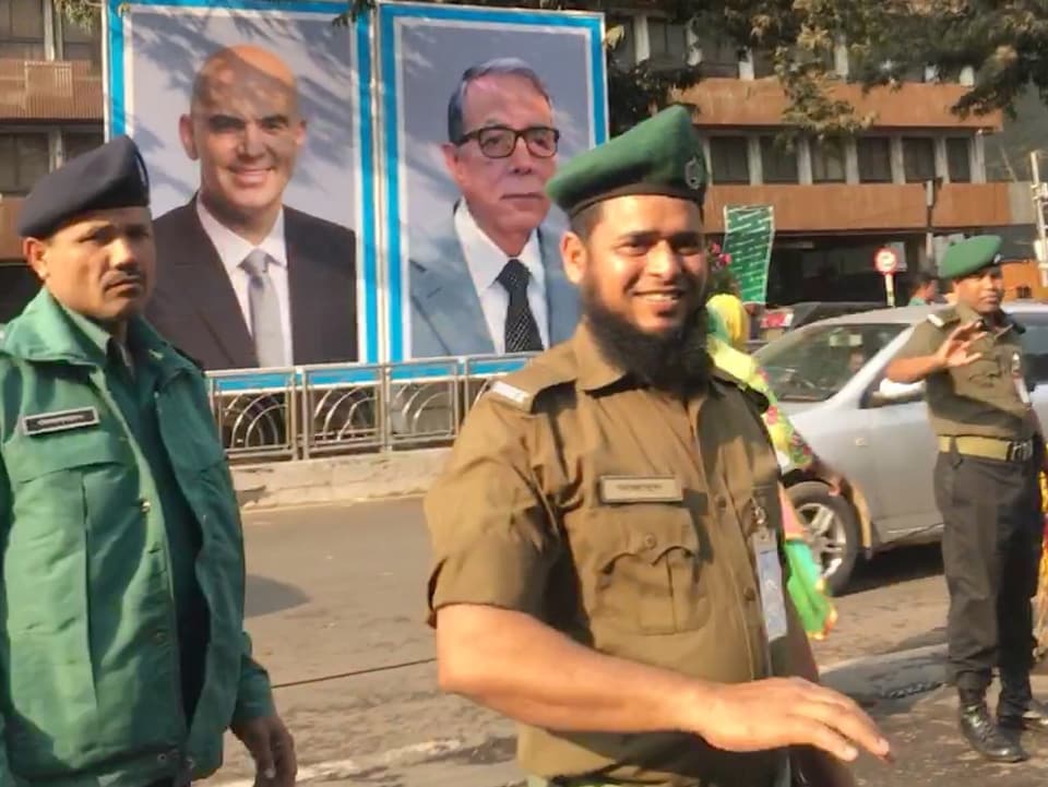 Sicherheitsleute sichern die Strassen in Dhaka. Auch an dieser Strasse ist ein grosses Plakat mit dem Foto von Alain Berset angebracht. (srf)