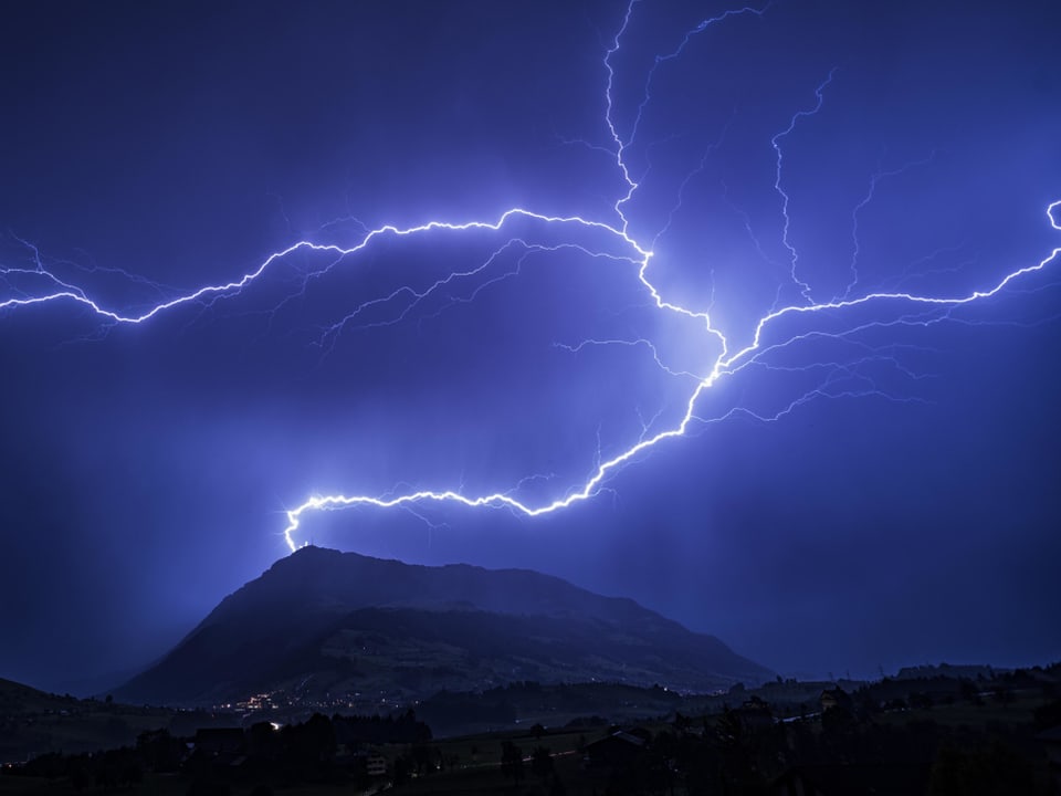 Bild in violett mit dunklem Berg, darauf eine Antenne, in die der Blitz einschlägt. Er erhellt den ganzen Nachthimmel. 