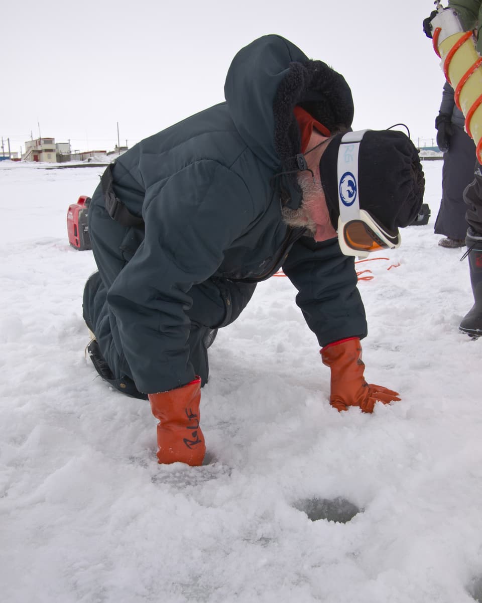 Rolf Gradinger kontrolliert und reinigt das Loch von Eismatsch, damit er weder Instrumente noch Planktonnetze verschmutzt oder verstopft.