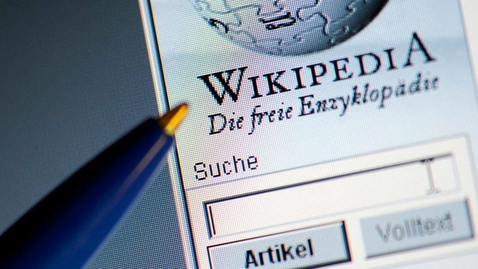 Ein Kugelschreiber zeigt auf einem Computerbildschirm auf die offene Wikipedia-Startseite mit Suchfenster.
