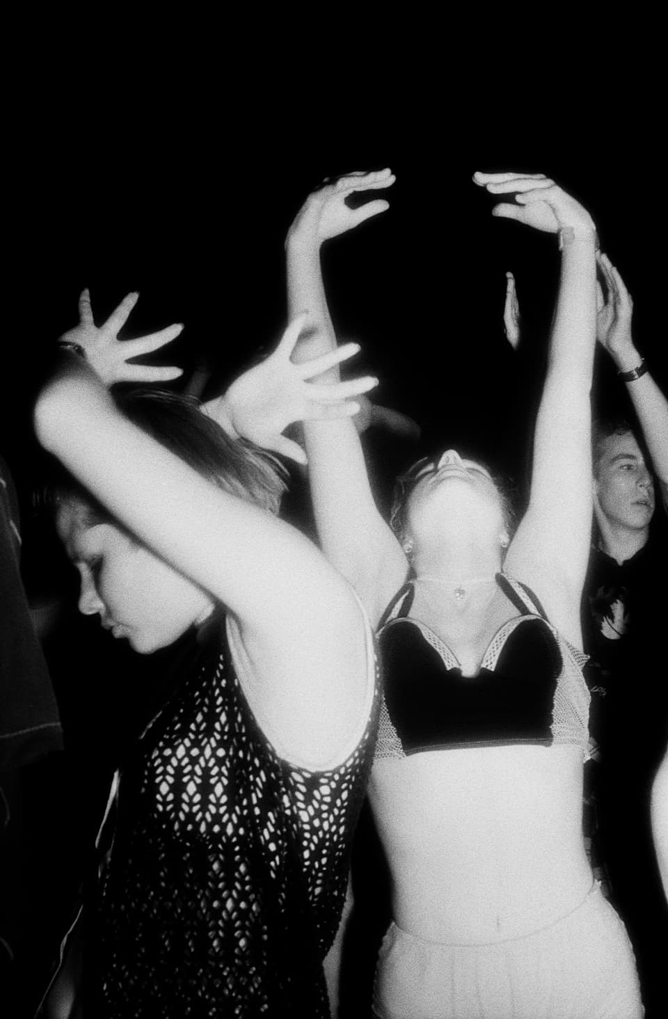 Man sieht mehrere junge Menschen beim Tanzen an einem Rave. Sie heben die Hände in die Luft.