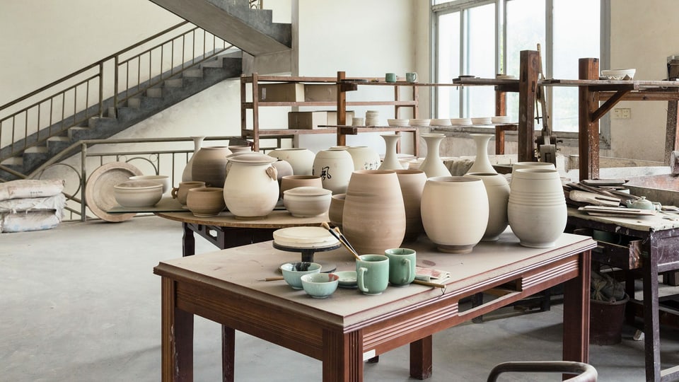 Arbeitsräume der Porzellan-Werkstatt. Viele Schalen, Vasen und Tassen auf einem Tisch.