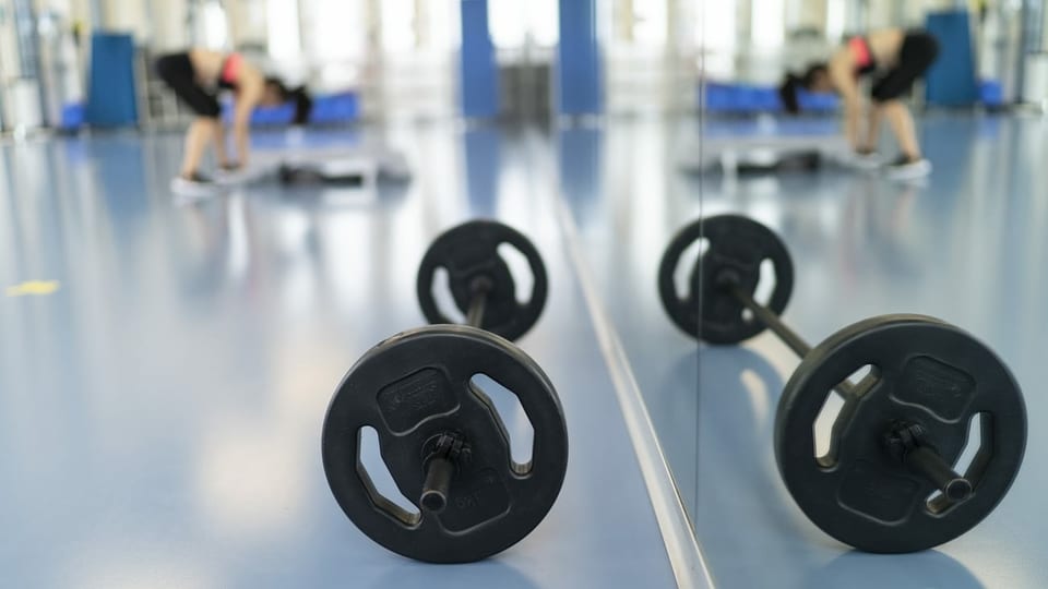 Hanteln im Fitnesszentrum vor Spiegtelwand, Frau dehnt sich.