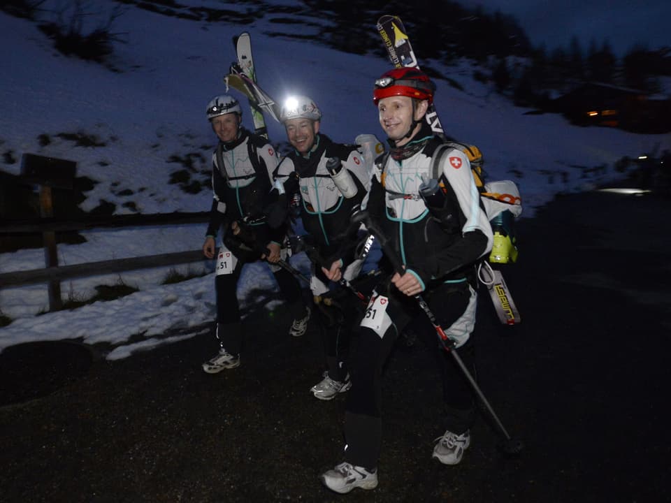 Patrouille mit drei Läufern mit Skiern auf dem Rücken. Sie marschieren in der Nacht bergauf. 