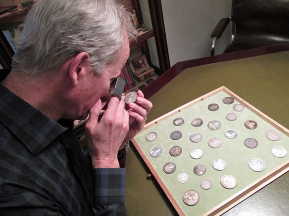 Mann betrachtet durch eine Lupe eine Münze.