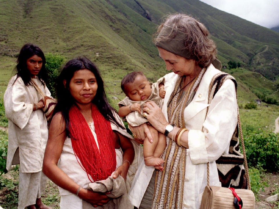 Königin Sofia mit Kind auf dem Arm und zwei Einwohnerinnen vor einem Berg.