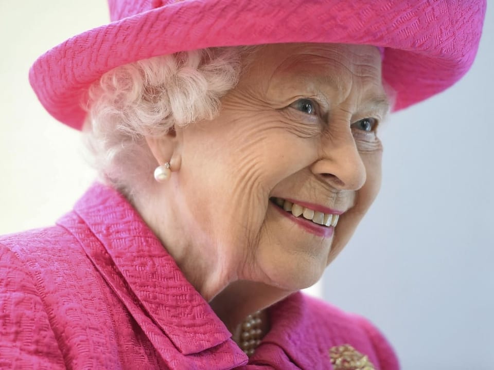 Die Queen trägt ein pinkes Kostüm und lächelt.