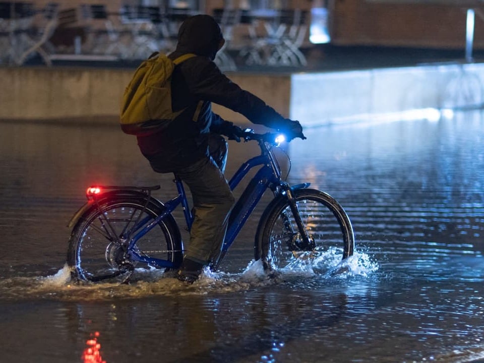 Fahrradfahrer gibt trotz 30 Zentimeter Wasser auf der Strasse nichtauf.