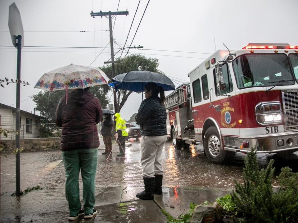 Zwei Frauen mit Schirm stehen im Regen neben einem grossen Feuerwehrauto,