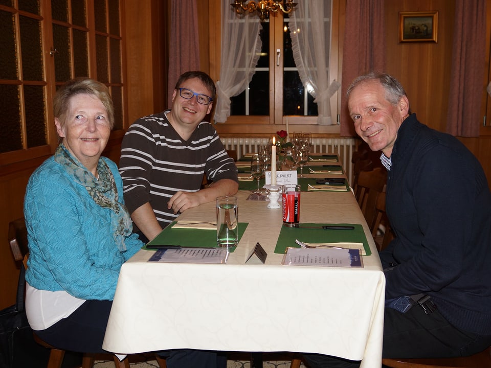 Eine Frau und zwei Männer an einem gedeckten Tisch in einer Gaststube.