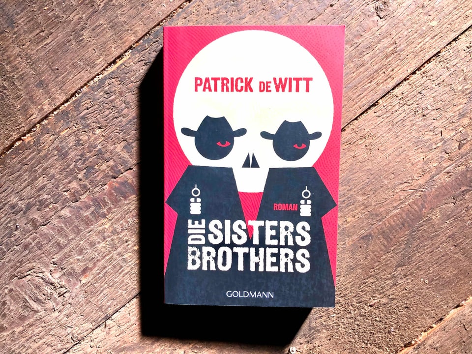 «Die Sisters Brothers» von Patrick deWitt liegen auf einem dunklen Dielenboden