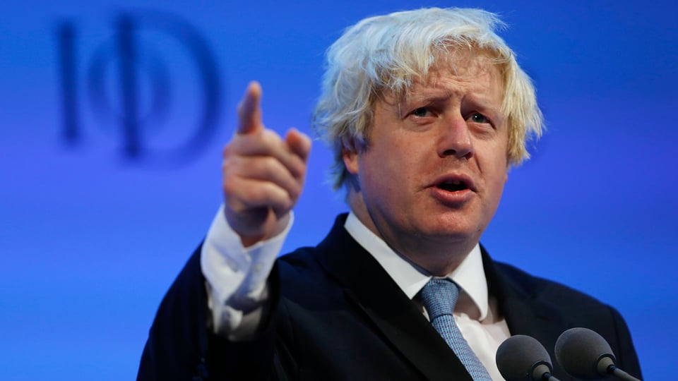 Boris Johnson spricht vor blauem Hintergrund in ein Mikrofon.