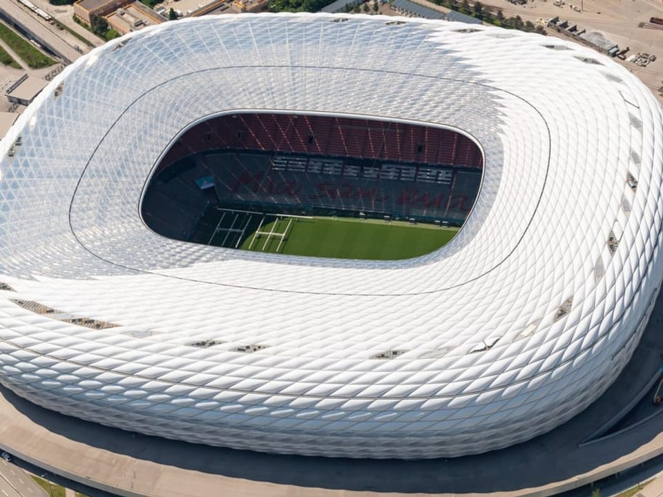 Viereckiges weisses Stadion auf grauem Asphalt.