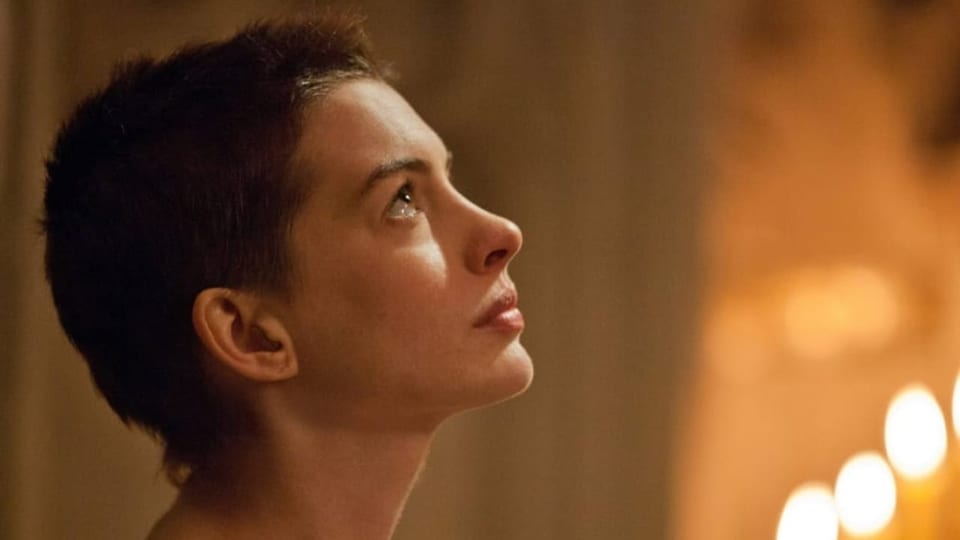 A woman with short hair looks up, candles behind her