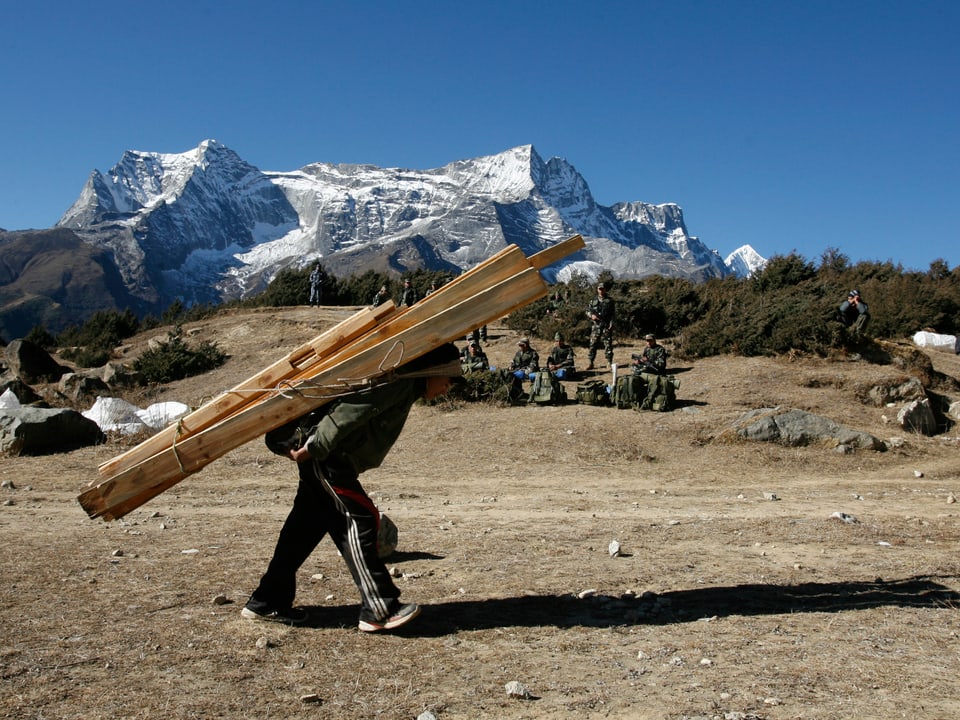 Mann schleppt Holz vor Himalaya-Panorama