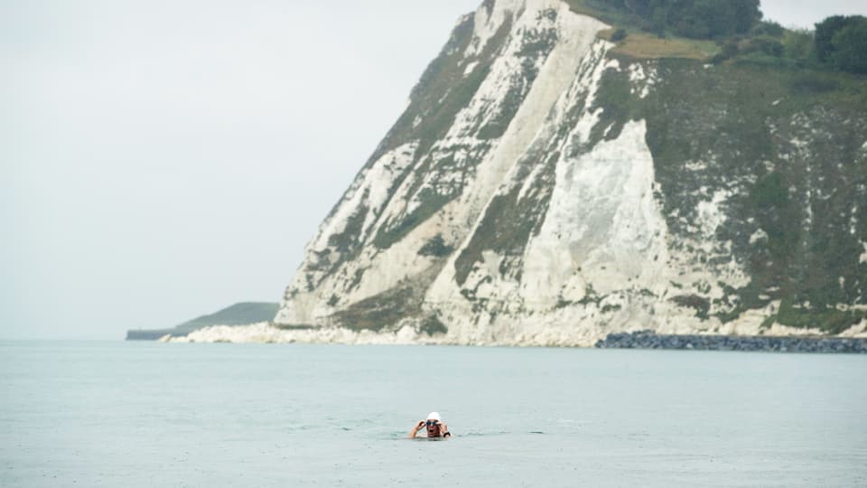 Ein Mann schwimmt im Meer. Im Hintergrund ist ein Gebirge.