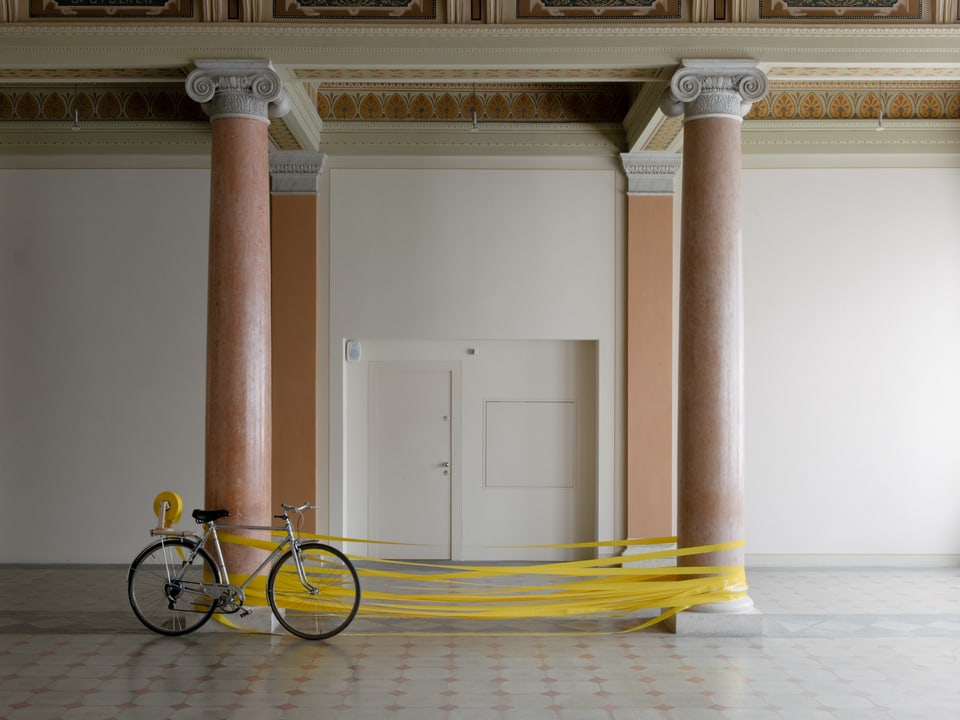 An zwei Säulen gelehnt steht ein Fahrrad, dahinter ist gelbes Band um die Säulen gewickelt.