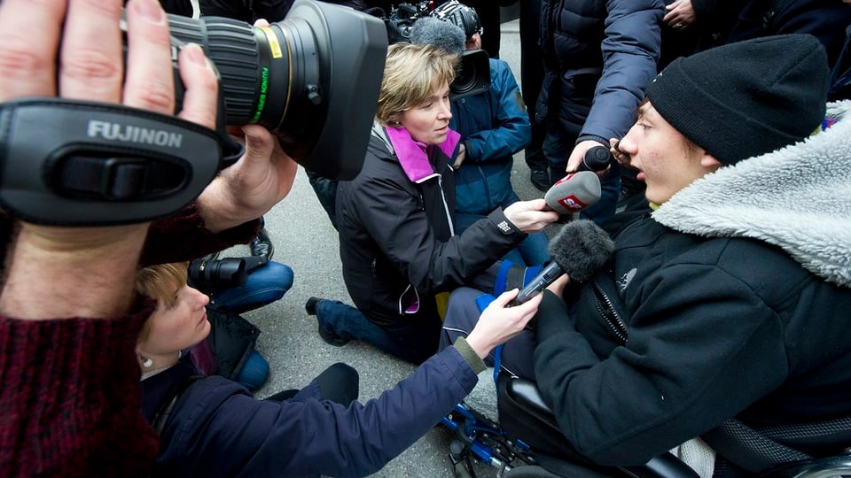 Luca im Rollstuhl von Journalisten umringt.