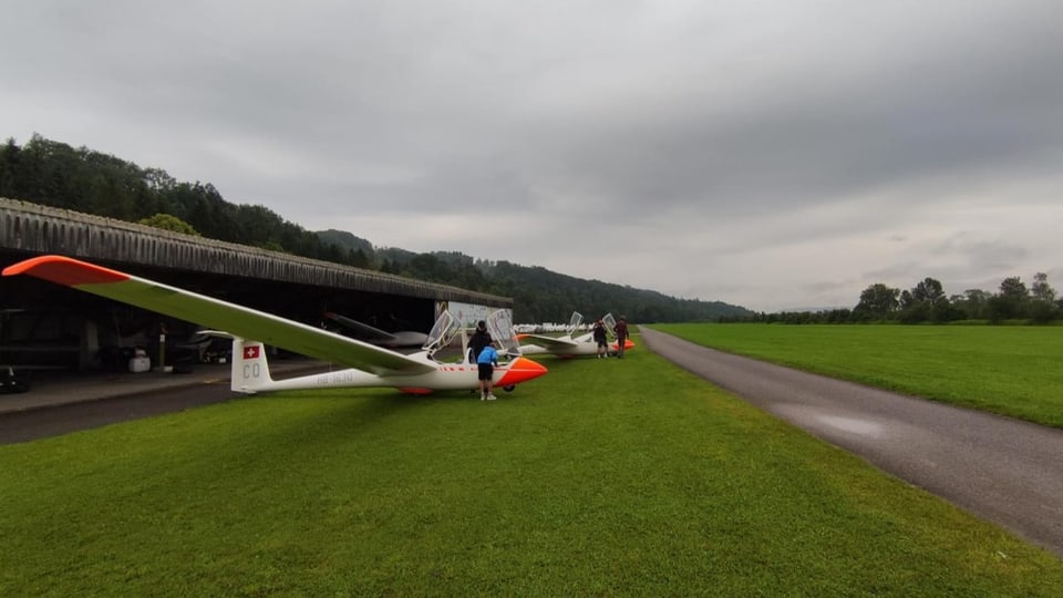 Zwei Segelflieger und Jugendlich auf der Wiese neben dem Flugfeld