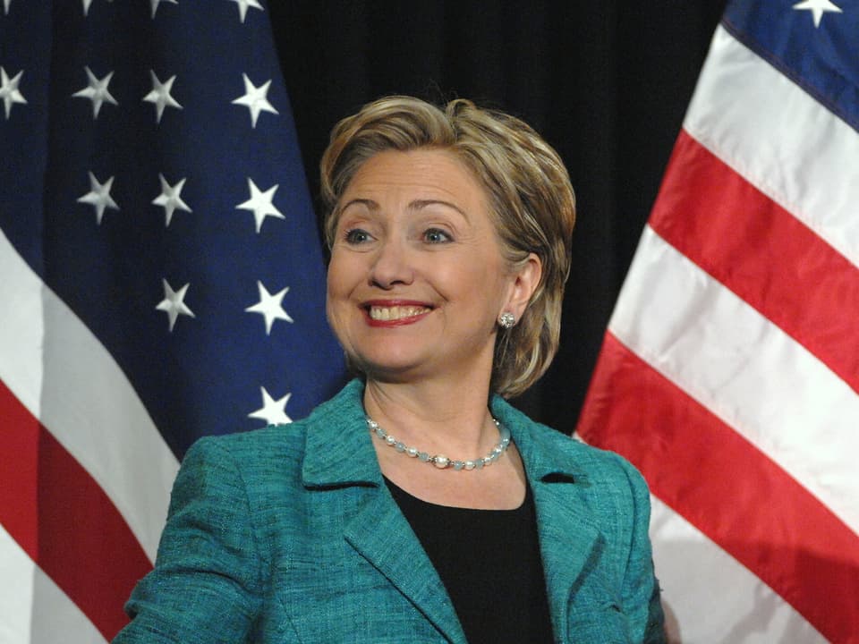 Hillary Clinton steht vor zwei US-Flaggen.