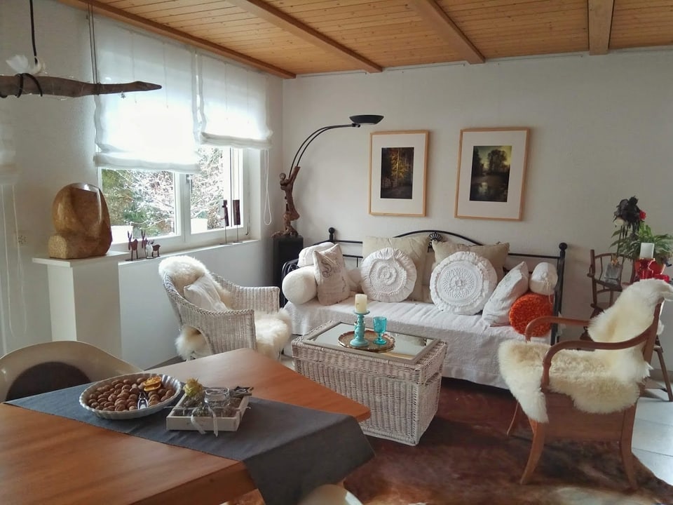 Ein Zimmer mit einem Holztisch, einem weissen Sofa und einem Stuhl mit Lammfell.