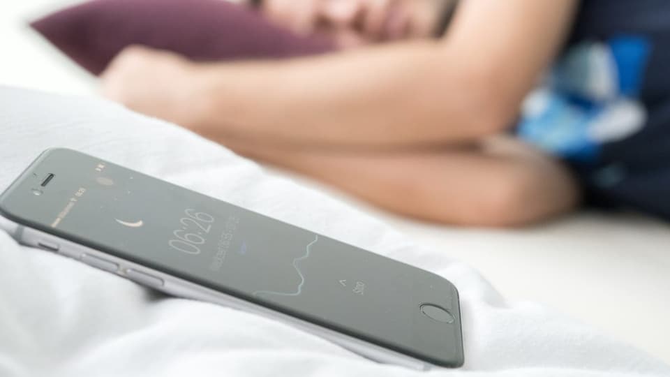 Schlaftracker aller Art: nächtliche Vermessung Ein Smartphone liegt neben einem schlafenden Mann.