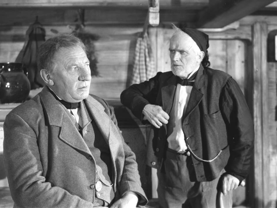 Zwei ältere Männer stehen in einem Bauernhaus.