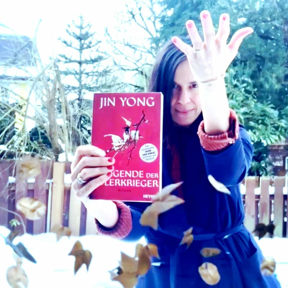 Annette König hält in der einen Hand «Die Legende der Adlerkrieger» von Jin Yong. Mit der anderen Hand erzeugt sie einen Wind, der Laubblätter in der Luft rotieren lässt. 