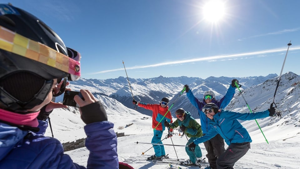Ein Skifahrer fotografiert vier Skifahrer auf der Piste mit einem Smartphone.