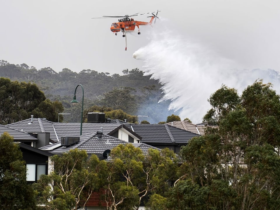 Ein Helikopter wirft Wasser über Häusern ab.