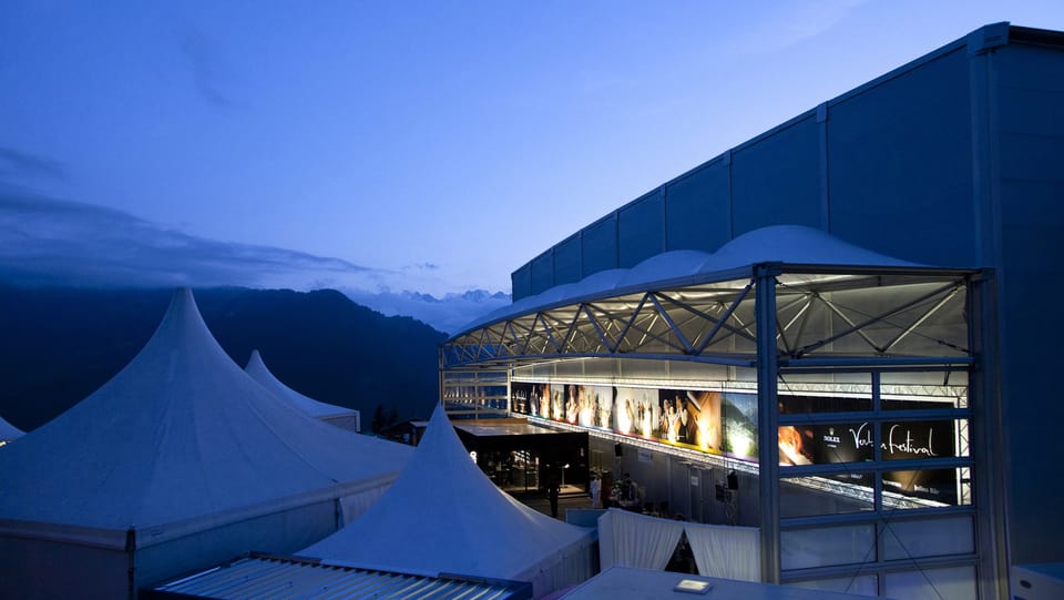 Blick auf den Konzertsaal, an dem unterschiedliche Veranstaltungen angeschlagen sind, vor der Alpen-Kulisse.