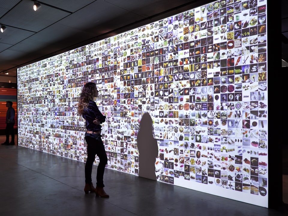 Eine Frau steht vor einer Wand, auf die Hunderte von Bildern projiziert sind.